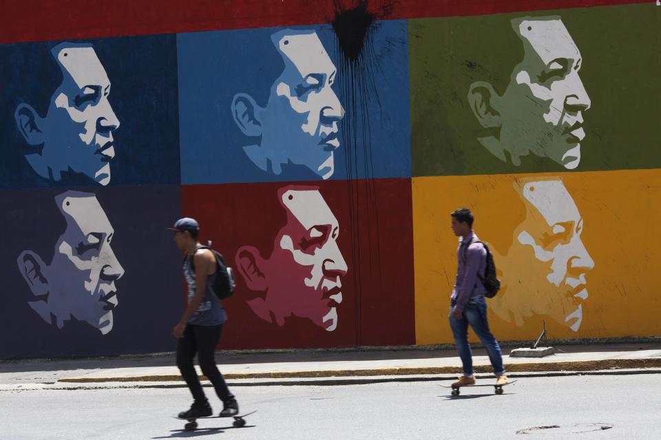Two men skate board past a mural of Venezuela's late President Hugo Chavez in downtown Caracas, Venezuela, Tuesday, March 4, 2014. He’s been dead a year, but Chavez’s face and voice are everywhere. On Wednesday, the country will mark Chavez's death, who died at age 58 on March 5, 2013. (AP Photo/Rodrigo Abd)