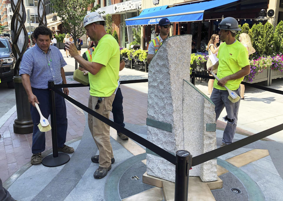 Sculptor Pablo Eduardo, left, and workers make final touches to stone pillars stand along Boylston Street after installation was finished, Monday, Aug. 19, 2019, in Boston to memorialize the Boston Marathon bombing victims at the sites where they were killed. Martin Richard, Krystle Campbell and Lingzi Lu were killed when bombs were detonated at two locations near the finish line on April 15, 2013. (AP Photo/Philip Marcelo)