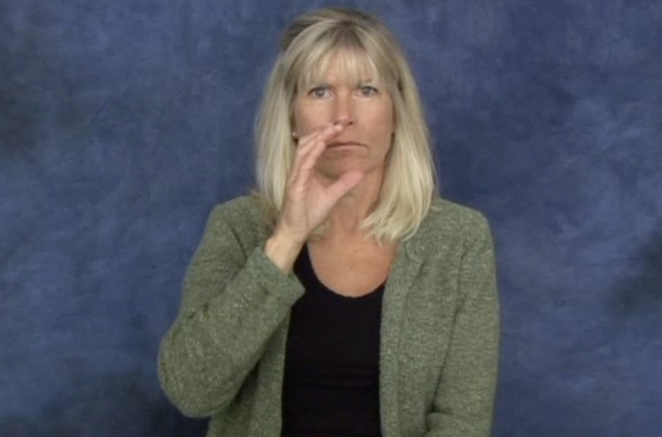 A woman with her hand up to her face making a motion similar to drinking.