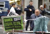 Peatones miran carteles desplegados fuera de una filial de Caja Madrid, del grupo Bankia (recientemente nacionalizado con pérdidas por el estado español) durante una protesta en la Plaza Celengue, en Madrid, el 9 de noviembre de 2012. (AFP | pedro armestre)