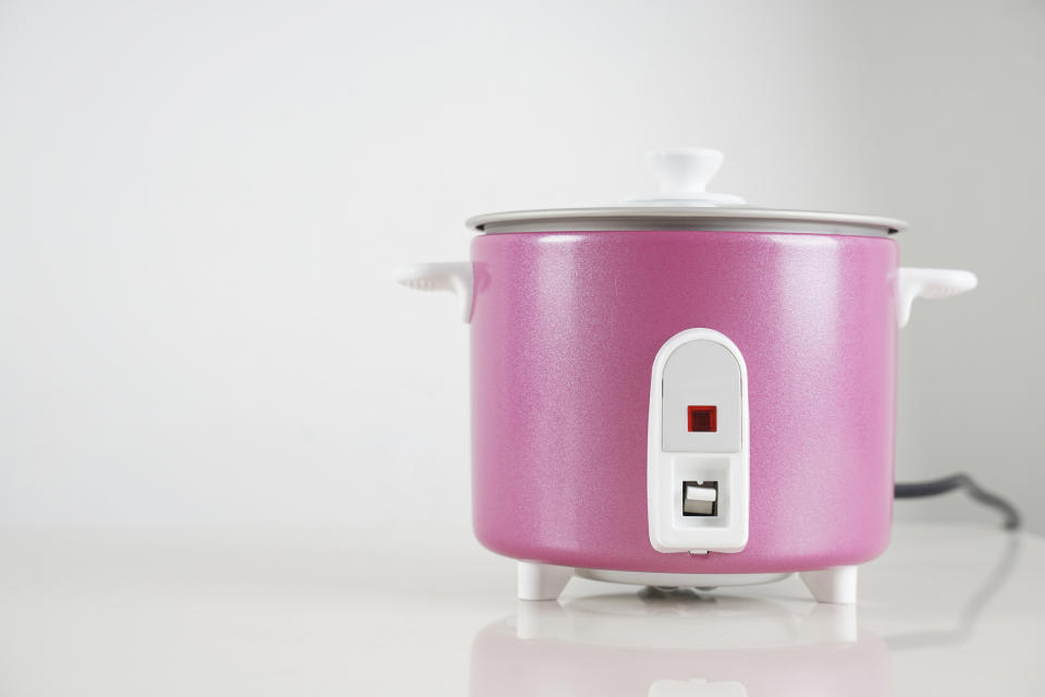 A pink rice cooker with a closed lid, switch on front, on a kitchen counter