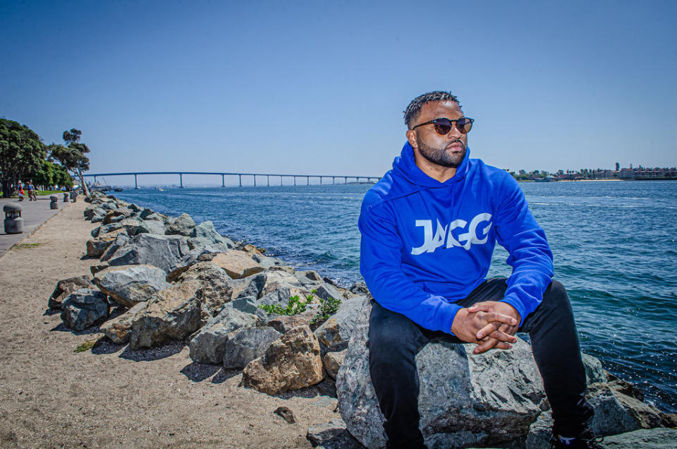 J French sits on a rot near the water with his hands clasped while wearing sunglasses.