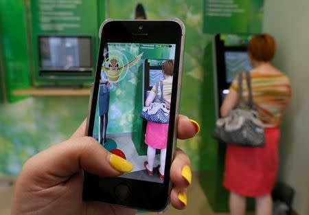 A woman plays the augmented reality mobile game "Pokemon Go" by Nintendo, as a visitor uses an automated teller machine (ATM) at a branch of Sberbank in central Krasnoyarsk, Siberia, Russia, July 20, 2016. REUTERS/Ilya Naymushin