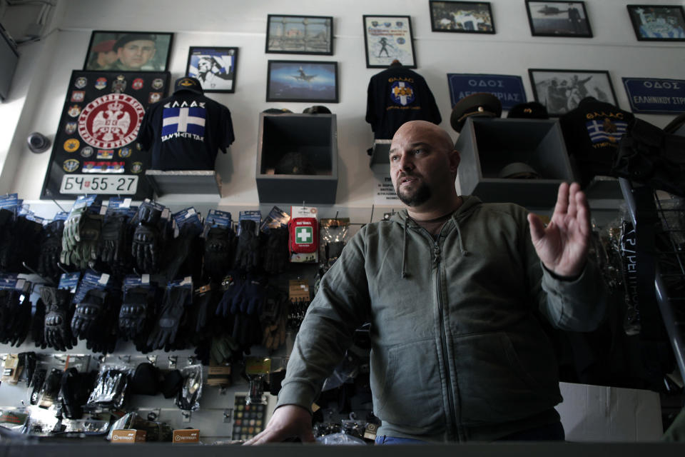 In this Oct. 26, 2012, photo, extreme far-right Golden Dawn party lawmaker Ilias Panagiotaros speaks in his shop in central Athens, explaining his party's policies and rejects accusations that it has been involved in racist attacks in Greece. Human rights and immigrant groups say there has been an increase in racist attacks in Greece over the last year, as the country struggles through a protracted financial crisis. On the top left a picture of Serbian warlord Zeljko Raznatovic Arkan is displayed.(AP Photo/Petros Giannakouris)