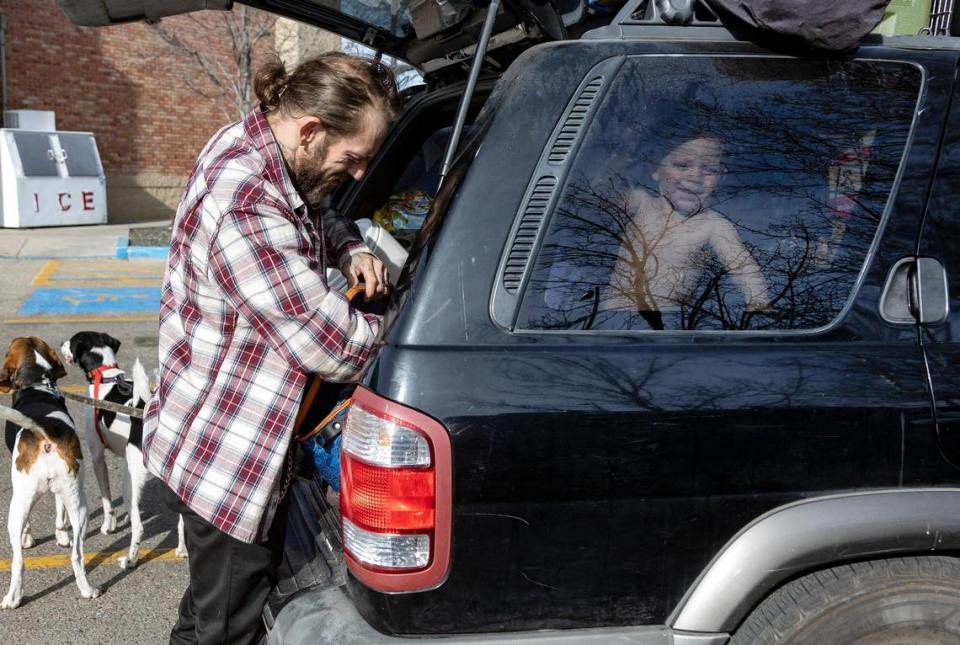 Thomas Lowder lets the dogs out of the car so he can pull out a set of clothes for Elijah, 1, who smiles out the back window while the family is parked in Boise in early February.
