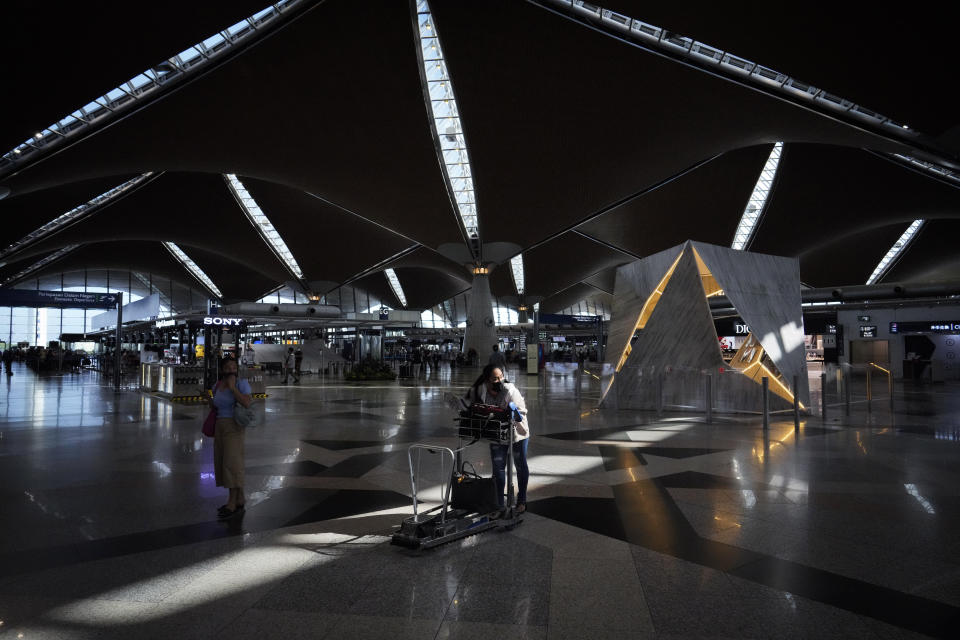 Travelers push their luggage to check in counter at Kuala Lumpur International Airport in Sepang, Malaysia, Friday, April 1, 2022. Malaysia's international borders open to foreigners on Friday and fully vaccinated travelers do not have to undergo quarantine. (AP Photo/Vincent Thian)