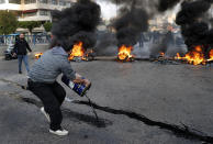 A protester pours oil in front of burning tires blocking a main highway that leads to Beirut's international airport during a protest against the increasing prices of consumer goods and the crash of the local currency in Beirut, Lebanon, Monday, Nov. 29, 2021. (AP Photo/Hussein Malla)