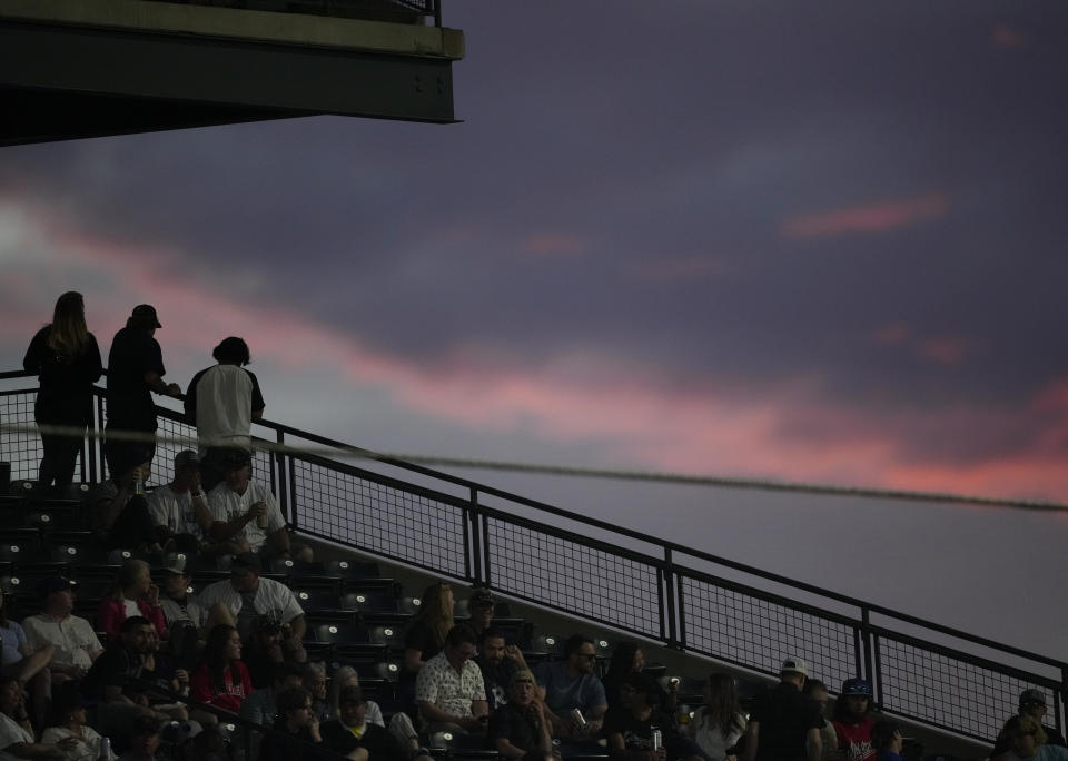 Fans look over the rail from the club level of Coors Field to watch the setting sun illuminate clouds, during the a baseball game between the Colorado Rockies and the Kansas City Royals on Saturday, May 14, 2022, in Denver. (AP Photo/David Zalubowski)