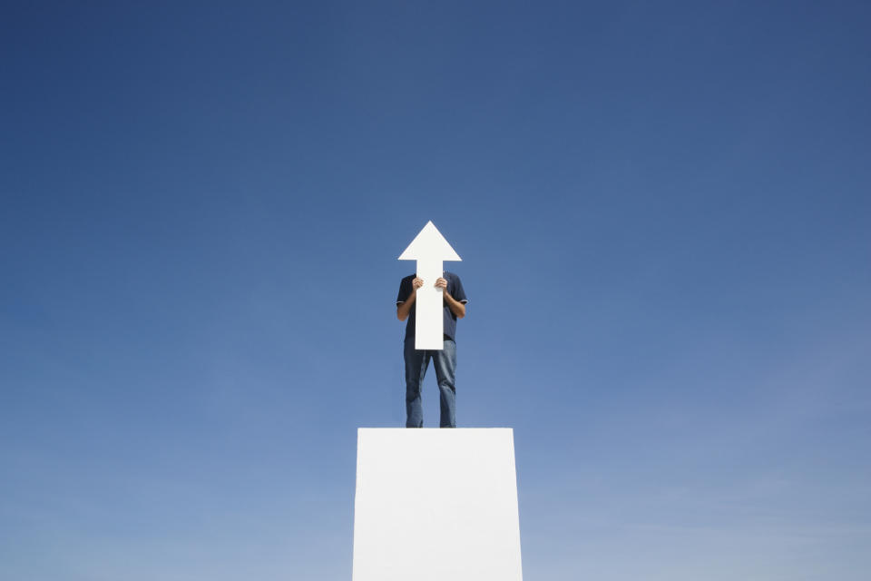 A man holding a cut out of a white arrow pointing up.