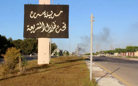 A sign which reads in Arabic, "The city of Sirte, under the shadow of Sharia" is seen as smoke rises in the background while forces aligned with Libya's new unity government advance on the eastern and southern outskirts of the Islamic State stronghold of Sirte, in this still image taken from video on June 9, 2016. Reuters TV/File Photo