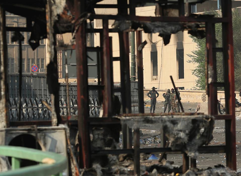 Iraqi security forces, seen through a burned police booth, close a bridge leading to the Green Zone while anti-government protesters gather for a demonstration in Baghdad, Iraq, Thursday, Oct. 3, 2019. Iraqi security forces fired live bullets and used tear gas against a few hundred protesters gathered in central Baghdad on Thursday, hours after a curfew was announced in the Iraqi capital on the heels of two days of deadly violence that gripped the country amid anti-government protests. (AP Photo/Hadi Mizban)