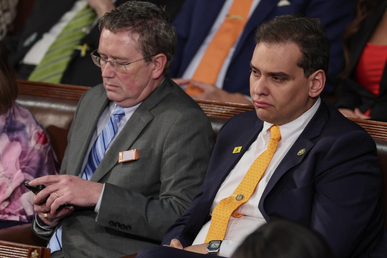 Rep. Thomas Massie looks at his cellphone, while George Santos sits with a disgruntled expression on his face.