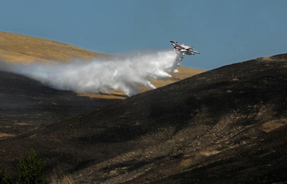 A fire fighting aircraft drops a load of water at a two-alarm wildfire that forced people from homes Monday afternoon just north of Benton City. There were no immediate details on the size or cause of the blaze.