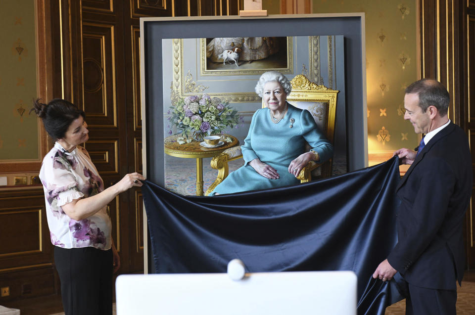 Undated handout photo released Saturday July 25, 2020, by the Royal Communications, showing the unveiling in London of a new portrait of Britain's Queen Elizabeth II by artist Miriam Escofet, left, with Simon McDonald, Permanent Under-Secretary of State for Foreign and Commonwealth Affairs and Head of the Diplomatic Service, right. The painting was commissioned by the Foreign and Commonwealth Office (FCO), as a 'lasting tribute to her service' to diplomacy. The Queen paid a virtual visit to the FCO via video call, to hear about their response to the COVID-19 outbreak and join the unveiling of the new portrait. (Foreign and Commonwealth Office via AP)