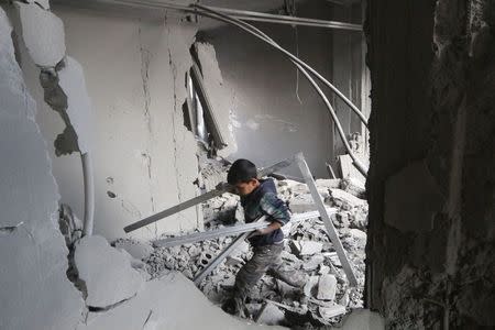 A boy collects items from among the debris of a school for the deaf and mute, destroyed in what activists said were overnight U.S.-led air strikes against the Islamic State, in Raqqa November 24, 2014. REUTERS/Nour Fourat