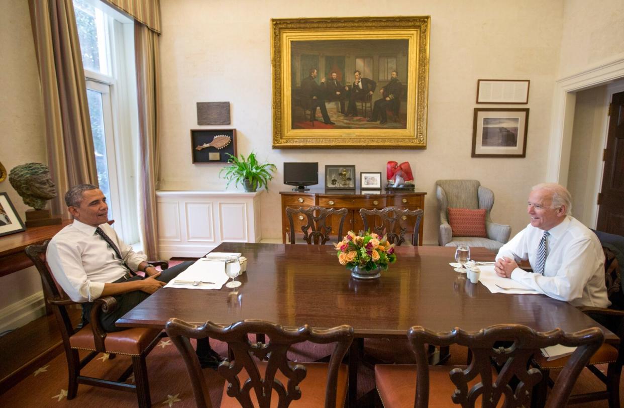 President Obama and Vice President Joe Biden smile at a dining room table in the White House.