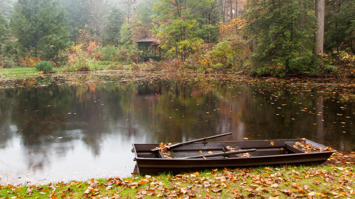 Tranquil view of a rowboat, pond and gazebo in autumn.