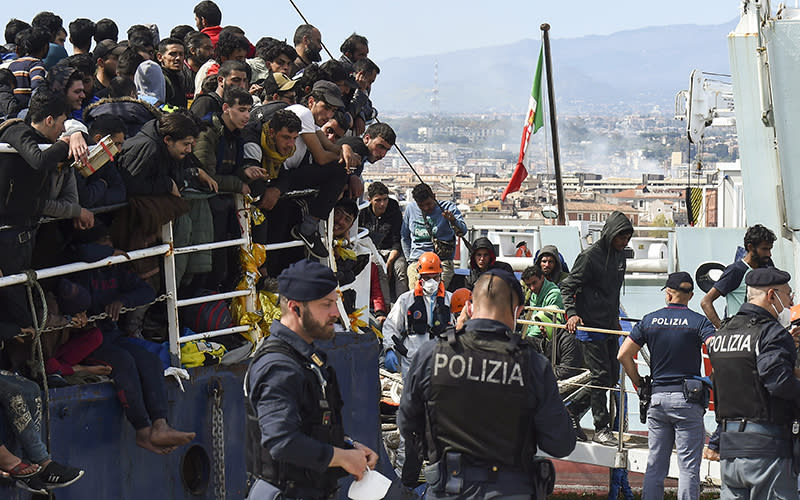 Migrants disembark from a ship in the Sicilian port of Catania as Italian police stand by