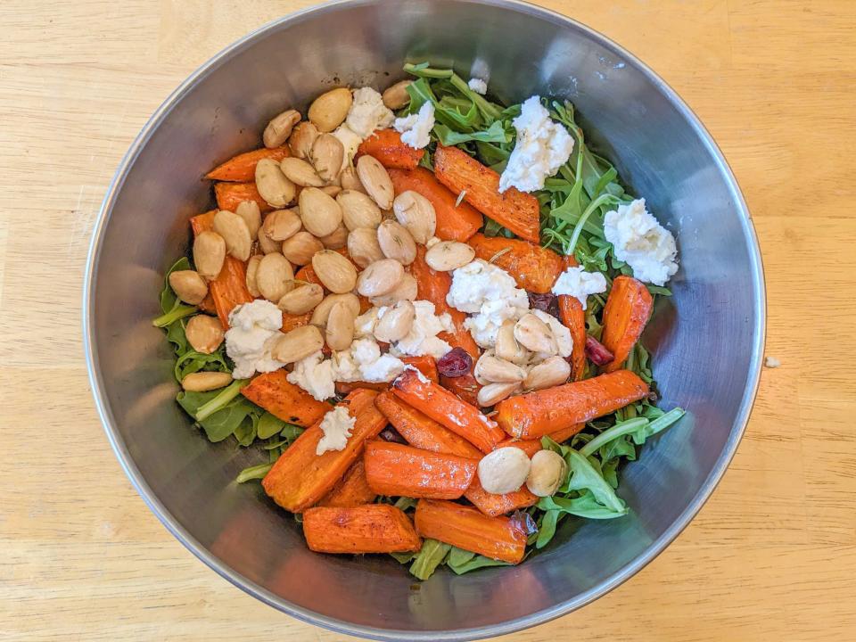 Bird's-eye-view of a metal bowl of almonds, arugula, cheese, cranberries, and pieces of carrots