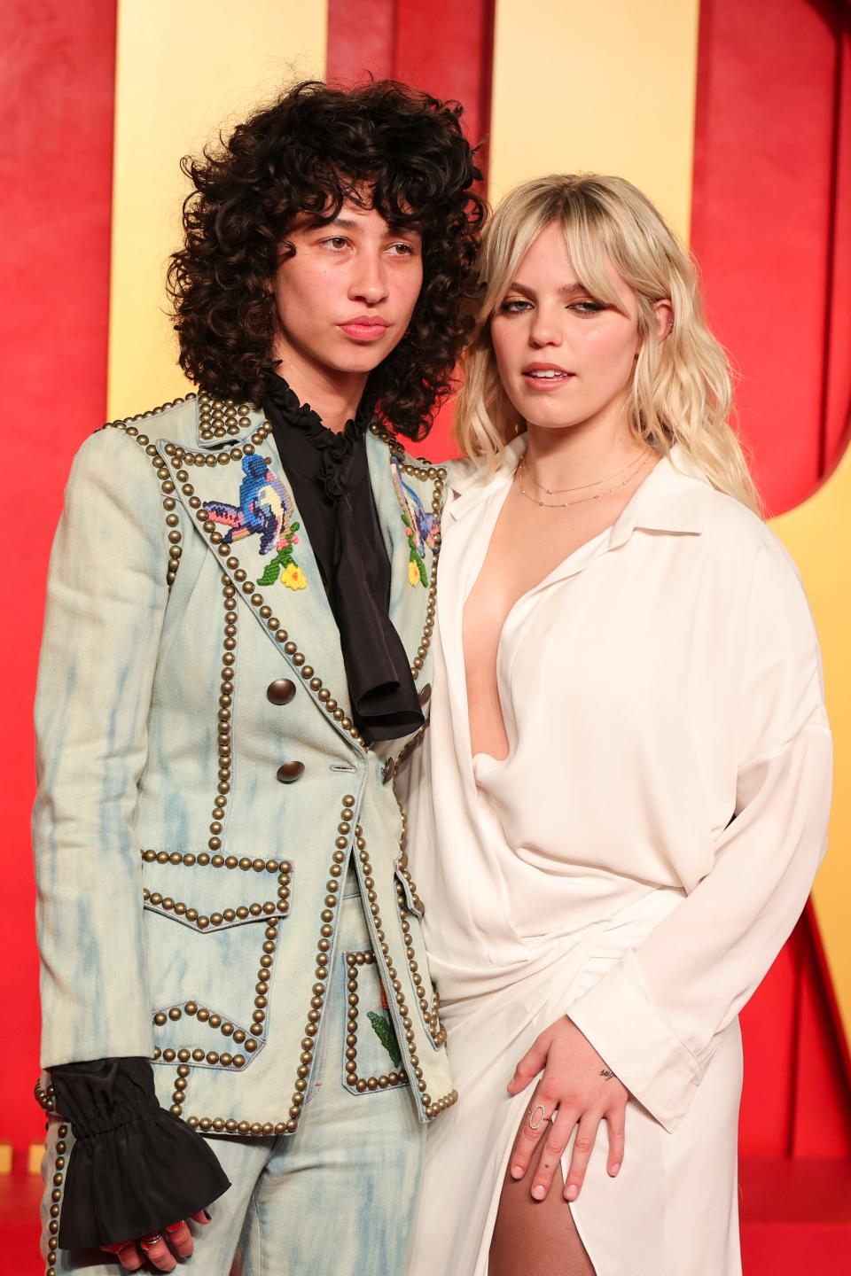 Reneé and Towa posing together, Towa in an embellished light pantsuit, Reneé in a plunging white outfit