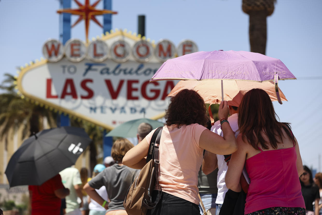 People stand under colorful umbrellas before a Las Vegas sign.