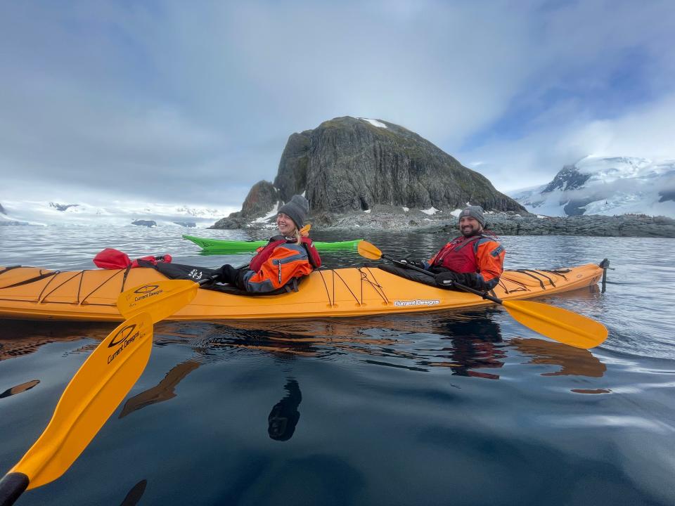 Alex and her husband smiling while in an orange kayak. They are wearing red coats, gray beanies, and life vests.