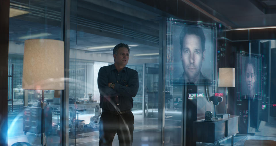 Mark Ruffalo as Bruce Banner stands in a lab with the faces of missing Avengers are projected on various digital screens.