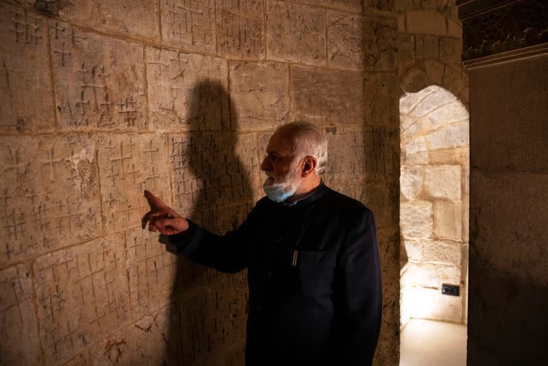 Father Samuel Aghoyan, the Armenian superior at the Church of the Holy Sepulchre touches crosses etched into the ancient stone wall of the Saint Helena chapel inside the church, during his interview with Reuters in Jerusalem's Old City
