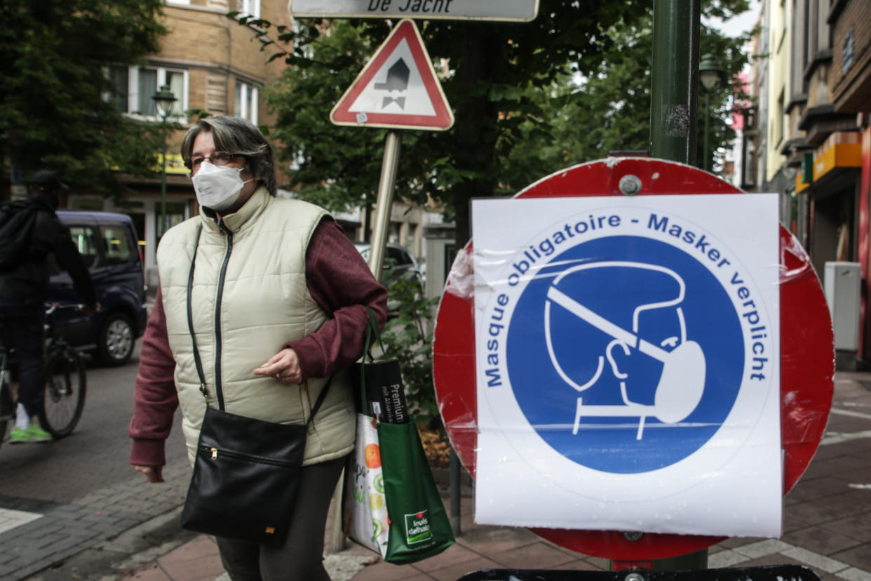 A woman wearing a face mask walks by a board bearing sanitary measures, on July 10 2020 in Brussels, amid the crisis linked with the Covid-19 pandemic caused by the novel coronavirus. - Wearing a face mask will become mandatory on July 10, 2020 in Belgian shops, cinemas, entertainment venues and other indoor spaces, the government announced. (Photo by Aris Oikonomou / AFP) (Photo by ARIS OIKONOMOU/AFP via Getty Images)