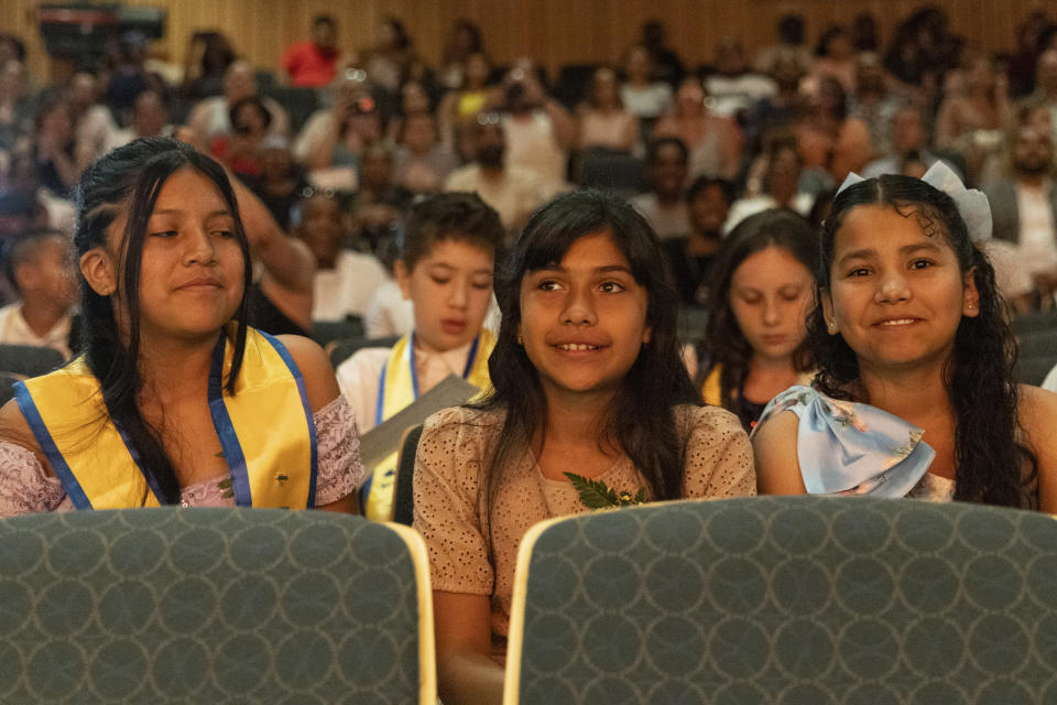 Sophia Prado, center, attends during a graduation ceremony at Trevor Day School, Friday, June 21, 2024, in New York. Thousands of migrant families in New York City are facing a summer of uncertainty for their school-aged children with a citywide limit of 60 days in a shelter before needing to reapply or find their own. (AP Photo/Jeenah Moon)