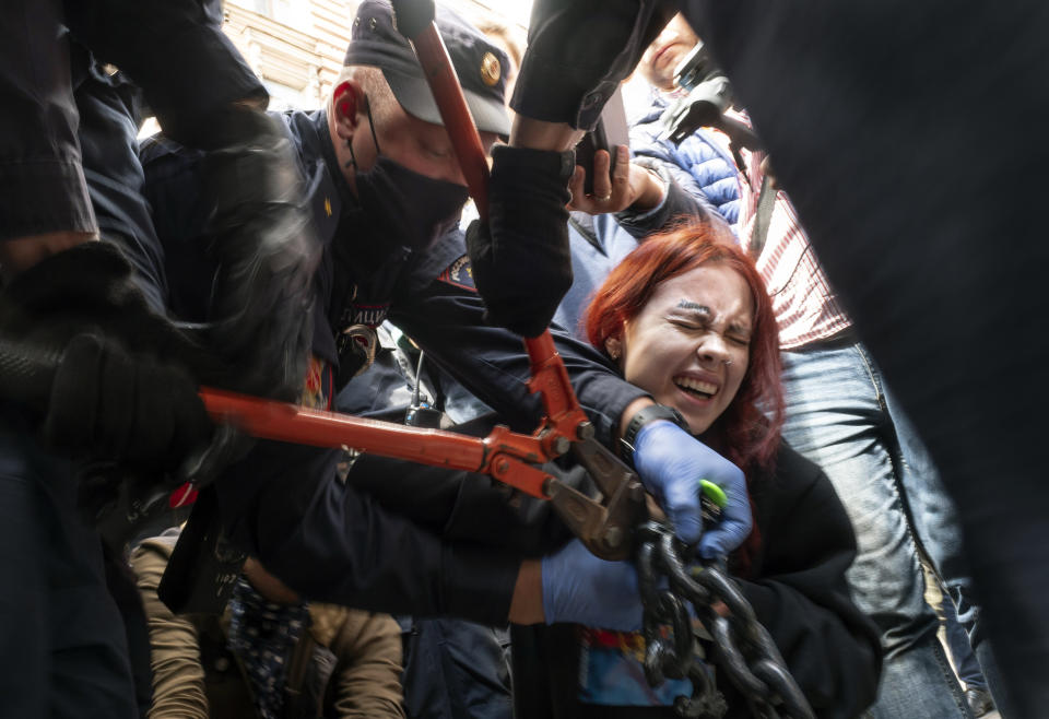 Police try to cut the handcuffs off a woman who handcuffed herself to a fence during a rally supporting Khabarovsk region's governor Sergei Furgal in St.Petersburg, Russia, Saturday, Aug. 1, 2020. Thousands of demonstrators rallied Saturday in the Russian Far East city of Khabarovsk to protest the arrest of the regional governor, continuing a three-week wave of opposition that has challenged the Kremlin. (AP Photo/Dmitri Lovetsky)