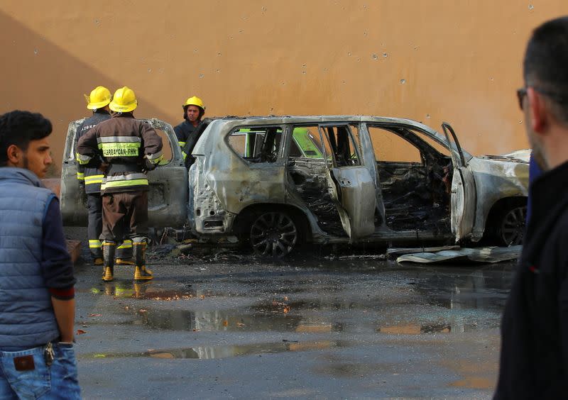 People gather near a burnt car hit by shelling in Barda