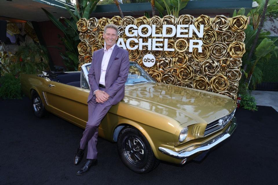 Golden Bachelor Gerry Turner leans against a gold old-school-style car.