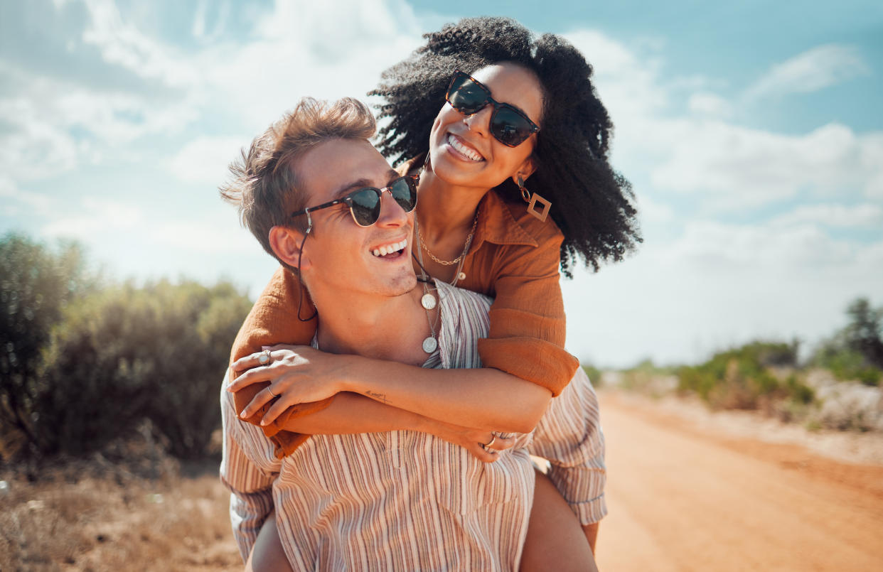 Love, happy and couple piggy back on road path in Arizona desert in USA for romantic getaway star sign. Interracial people dating smile while enjoying summer romance on travel holiday adventure together.