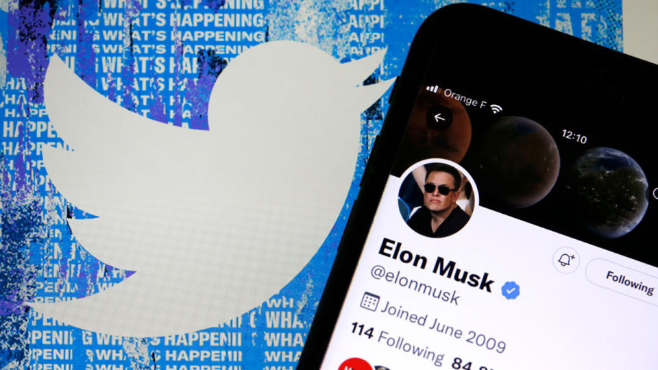 Elon Musk Twitter-fiókja egy iPhone képernyőjén jelenik meg a Twitter webhely kezdőlapja előtt