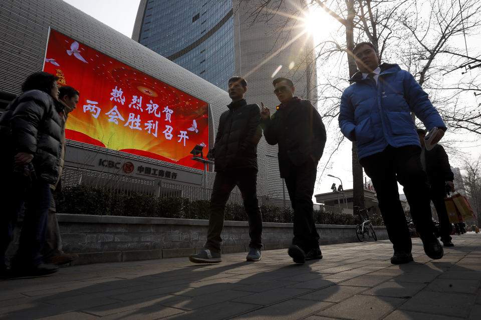 Chinese people walk past a giant screen showing "Welcome the annual session of two meetings held victory" on display outside a bank office building in Beijing, Friday, March 1, 2019. Thousands of delegates from around China are gathering in Beijing for next week's annual session of the country's rubber-stamp legislature and its advisory body. The event is more a chance for the authoritarian ruling Communist Party leadership to directly communicate its message than for actual debate or passage of laws. (AP Photo/Andy Wong)