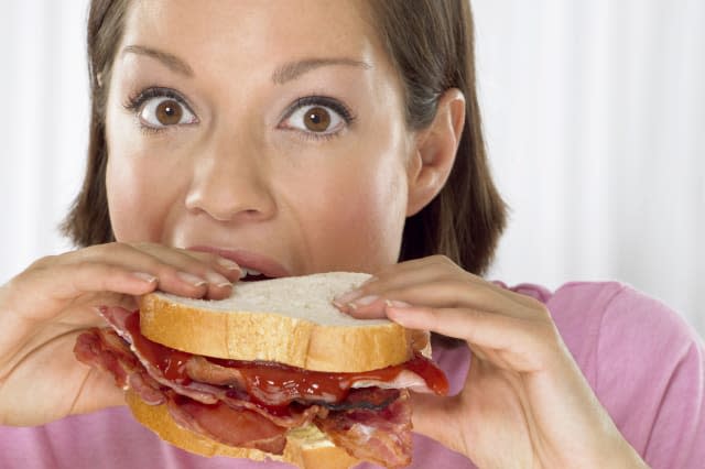 Portrait of a Young Woman Biting into a Bacon Sandwich