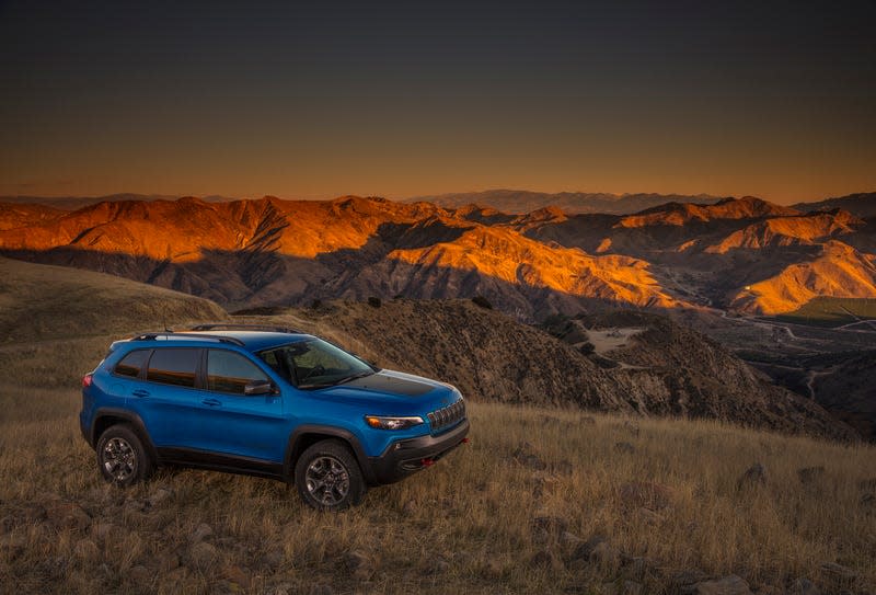 A Jeep Cherokee in blue parked in front of a beautiful view of mountains