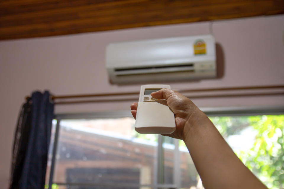 Woman hand holding remote control directed to air conditioner adjust cold temperature, close up.
Woman hand using remote control open or close air conditioning system in house, Health and energy saving concept.