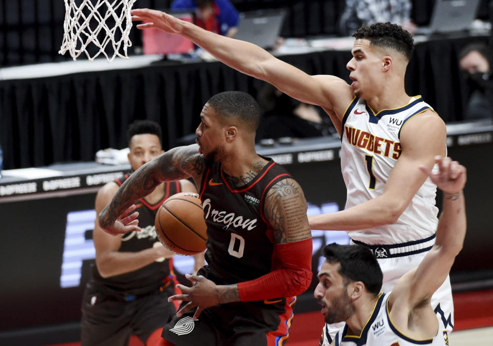 Portland Trail Blazers guard Damian Lillard, center, passes the ball behind his back to guard CJ McCollum, left, as Denver Nuggets forward Michael Porter Jr., right, defends during the first half of an NBA basketball game in Portland, Ore., Sunday, May 16, 2021. (AP Photo/Steve Dykes)