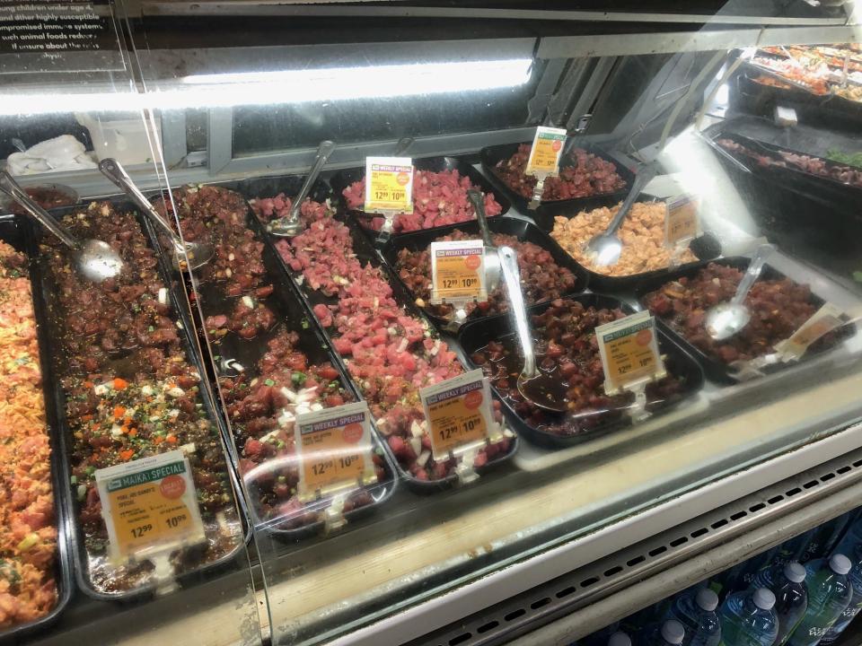 Several types of poke, including spicy ahi and soy-sauce, sit in trays in a deli cooler case at Snack N Save in Hilo