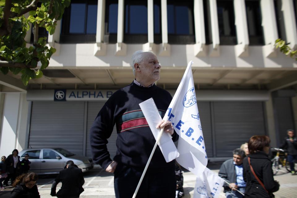 A protester holds a labor union flag during a protest from the confederation of Professionals, Craftsmen and Merchants against a new austerity bill that will be discussed in Parliament, in Athens, Sunday, March 30 2014. The measures demanded by bailout lenders will be voted on late Sunday, and would liberalize several retail sectors. They include plans to grant supermarkets permission to set up in-store pharmacies, scrap price limits on books and allow a longer shelf-life for milk. (AP Photo/Kostas Tsironis)