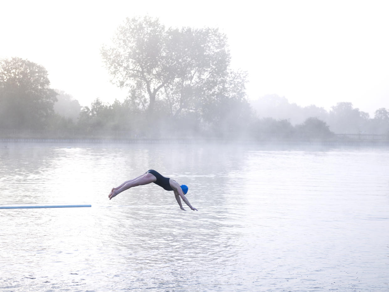 Woman jumping off diving board into lake, side view