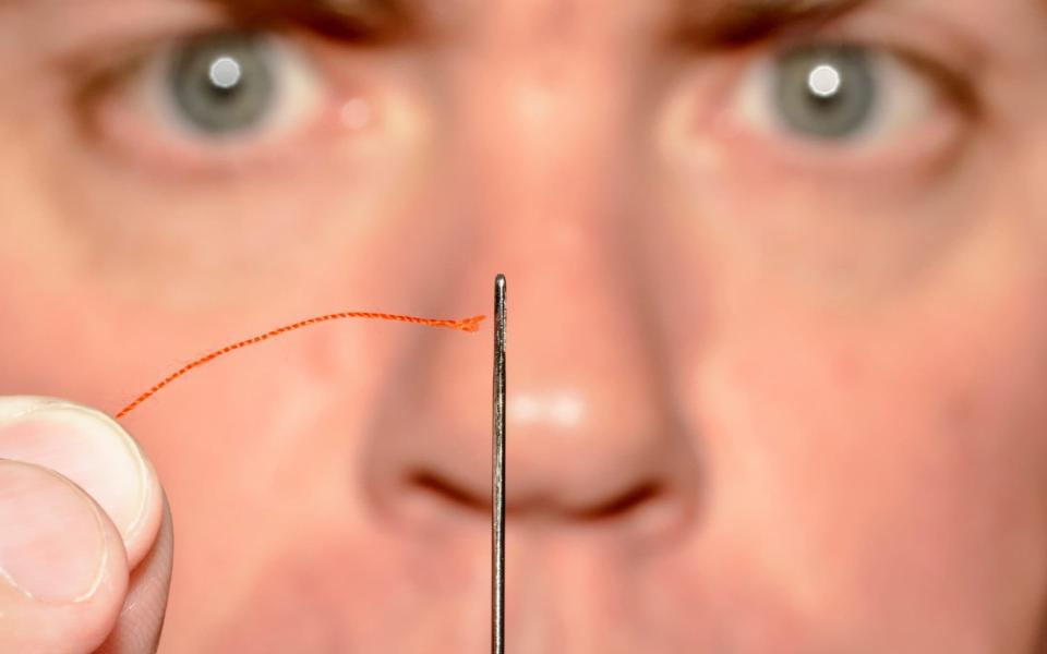 Man concentrating while threading cotton thread through the eye of a needle - Geoff Smith / Alamy 