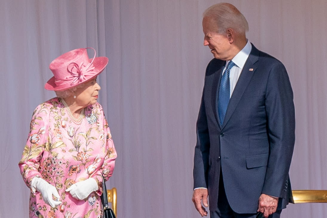 President Biden, looking convivial, speaks to a slightly skeptical Queen Elizabeth, in pink silk outfit and pink straw hat.
