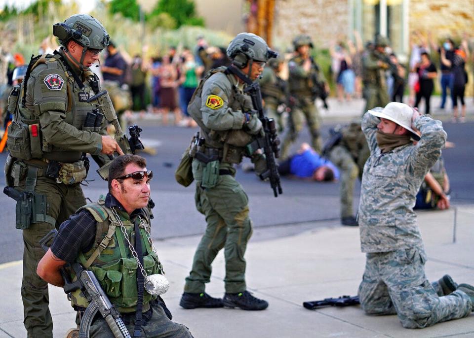 Albuquerque police detain members of the New Mexico Civil Guard, an armed civilian group, following the shooting of a man during a protest over a statue of Spanish conqueror Juan de Oñate on Monday, June 15, 2020, in Albuquerque. A confrontation erupted between protesters and a group of armed men who were trying to protect the statue before protesters wrapped a chain around it and began tugging on it while chanting: "Tear it down." One protester repeatedly swung a pickax at the base of the statue. Moments later a few gunshots could be heard down the street and people started yelling that someone had been shot.