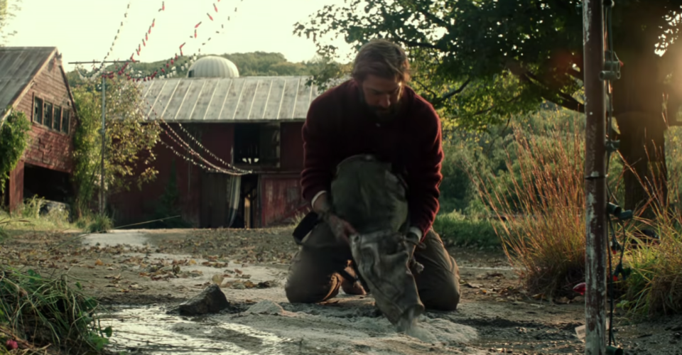 John Krasinski in A Quiet Place, looking rugged and digging in front of a farm house