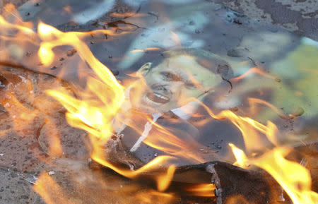 A poster of French President Emmanuel Macron is set on fire during a protest against western air strikes on Syria, in Simferopol, Crimea April 15 , 2018. REUTERS/Pavel Rebrov