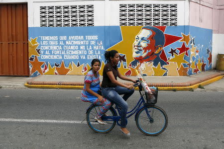 Women ride past a mural depicting late Venezuela's President Hugo Chavez in front of his childhood house, in Sabaneta, in the state of Barinas, November 19, 2015. REUTERS/Marco Bello.