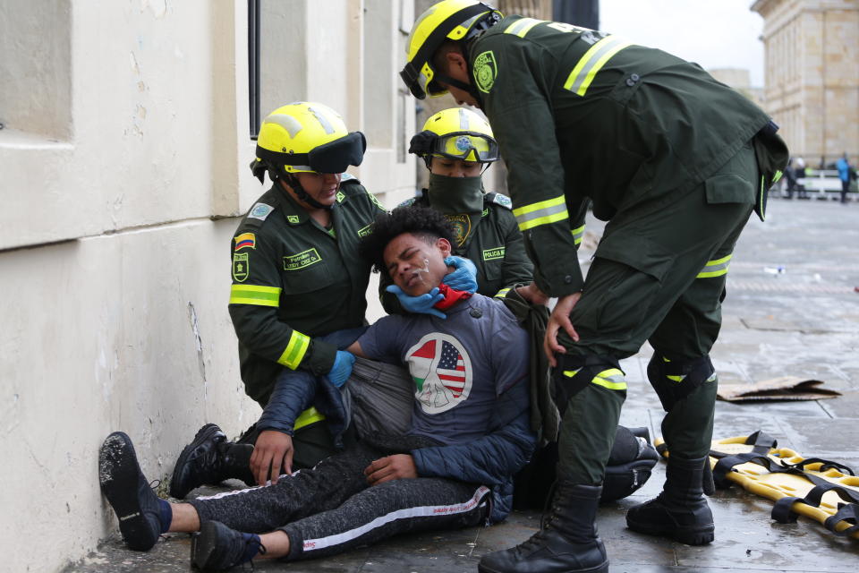 Police attend an anti-government protester affected by tear gas during clashes in downtown Bogota, Colombia, Friday, Nov. 22, 2019. Labor unions and student leaders called on Colombians to bang pots and pans Friday evening in another act of protest while authorities announced three people had died in overnight clashes with police after demonstrations during a nationwide strike. (AP Photo/Ivan Valencia)